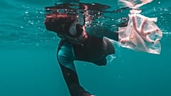 A diver captures plastic waste floating in the ocean.