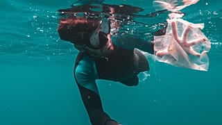A diver captures plastic waste floating in the ocean.