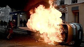 A firefighter tries to extinguish a burning car on place d'Italie in Paris on November 16, 2019