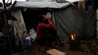 لاجئ سوري يعانق ابنه بالقرب من خيمة للجوء في اليونان 