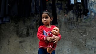 Palestinian girl of Radhi family holds a doll outside her family home in Al-Shati refugee camp in Gaza City