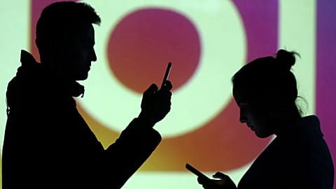 Silhouettes of mobile users are seen next to a screen projection of Instagram logo