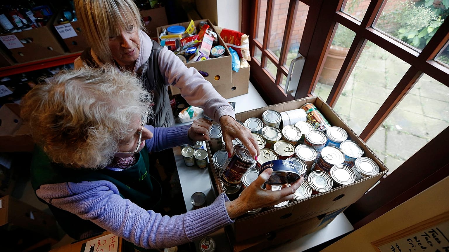 Food bank volunteers Janette Pasquali, top, and Diana Grant sort cans of food at a food bank in Bromley, south London, Tuesday, Oct. 15, 2013