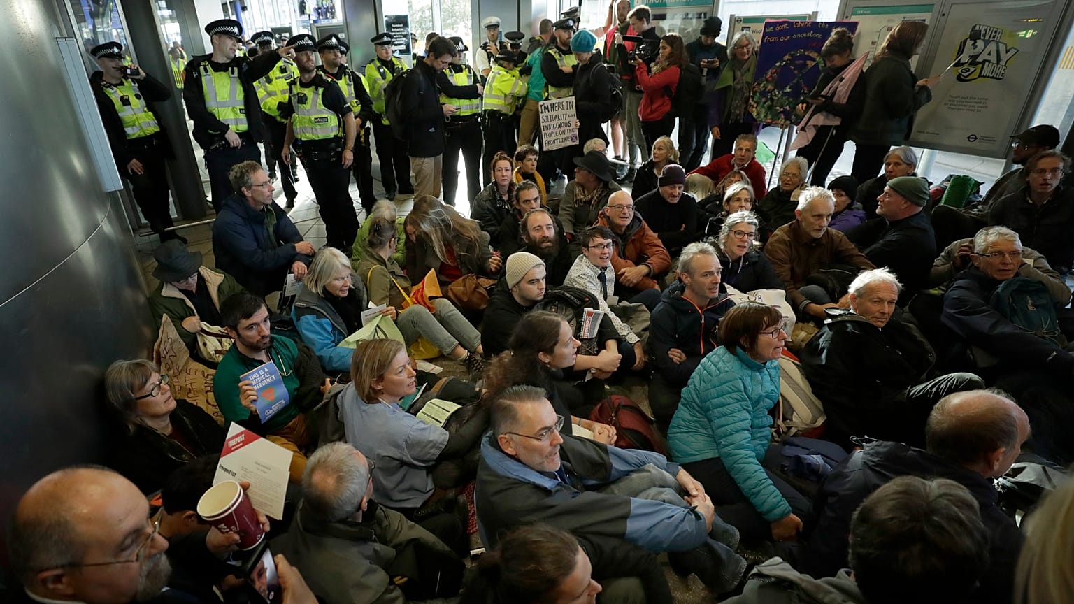 Police Officers stand guard as Extinction Rebellion demonstrators peacefully block an entrance to City Airport in London, Thursday, Oct. 10, 2019.