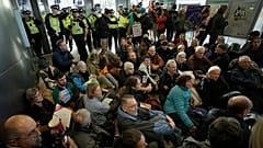 Police Officers stand guard as Extinction Rebellion demonstrators peacefully block an entrance to City Airport in London, Thursday, Oct. 10, 2019.