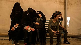 نساء مرتبطات بمقاتلي جماعة الدولة الإسلامية يجلسن بجانب حارسات من قوات سوريا الديمقراطية في مخيم الهول يونيو 2019