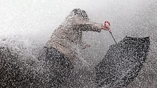 A woman tries to keep her balance as waves hit the seawall in Biarritz, southwestern France, Sunday, Dec.22, 2019