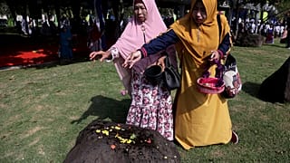 Women sprinkle flowers on a stone marking the mass grave for the victims of 2004 tsunami, during a commemorative service in Banda Aceh, Indonesia, Dec. 26, 2018.