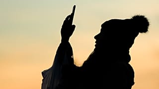 A person silhouetted against the evening sky makes a photo with a smartphone in Philadelphia, Thursday, Dec. 12, 2019.