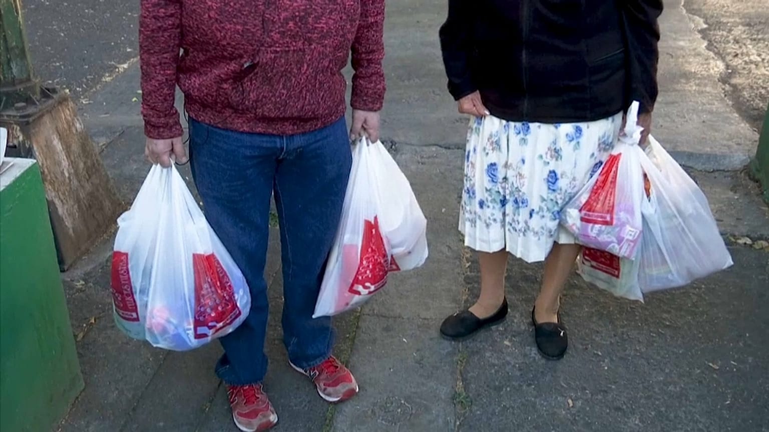 Dos mexicanos cargan bolsas de plástico tras salir de la compra