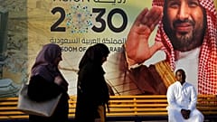 سعوديون أمام لافتة لولي العهد السعودي محمد بن سلمان ورؤية 2030، في مركز تجاري في جدة، المملكة العربية السعودية.
