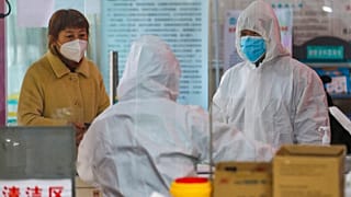 Medical workers in protective gear talk with a woman suspected of being ill with a coronavirus at a community health station in Wuhan in central China's Hubei Province