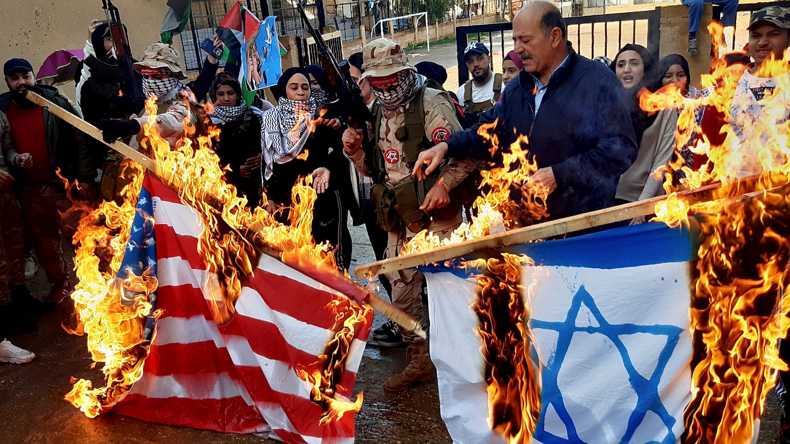 فلسطينيون مسلحون ومدنيون يحرقون علمي إسرائيل والولايات المتحدة خلال احتجاج في مخيم عين الحلوة في لبنان 