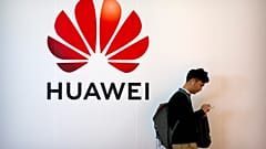 A man uses his smartphone as he stands near a billboard for Chinese technology firm Huawei at the PT Expo in Beijing