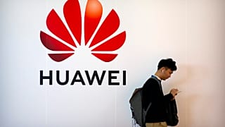 A man uses his smartphone as he stands near a billboard for Chinese technology firm Huawei at the PT Expo in Beijing