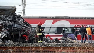 The wreckage of the locomotive of a high-speed train crammed onto another train on adjacent tracks, as the rest of train is seen in the background, after it derailed. Italy.