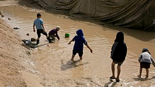 FILE - In this March 31, 2019 file photo, children play in a mud puddle in the section for foreign families at Al-Hol camp in Hasakeh province, Syria.