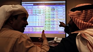 صورة من الأرشيف- يتحدث تجار سعوديون وهم يتابعون شاشة تعرض قيم سوق الأسهم السعودية