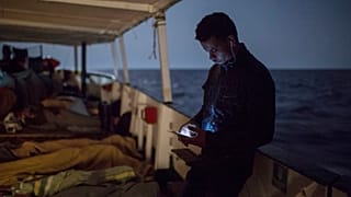 A migrant checks is cellular phone as other sleep on the deck of the Open Arms aid boat, of Proactiva Open Arms Spanish NGO, Sunday, July 1, 2018.