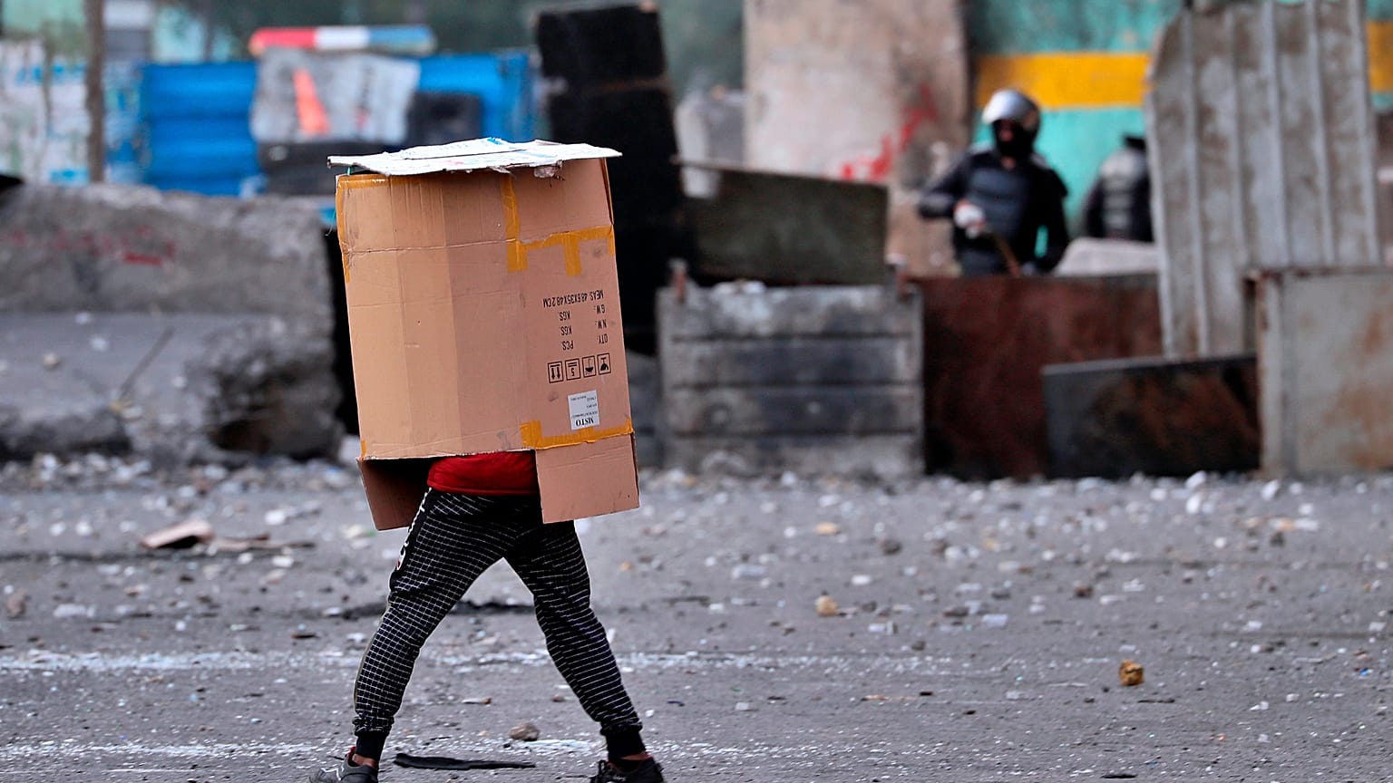 A protester covers his body while security force use slingshots to disperse anti-government protesters during clashes in downtown Baghdad, Iraq