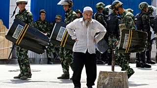 July 8, 2009, file photo, paramilitary police walk past an elderly ethnic minority man in Urumqi, western China's Xinjiang region.