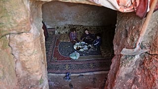 Members of a family of internally displaced Syrians eat together in an underground shelter where several families from Aleppo and Idlib provinces are taking refuge.