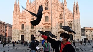 A man wearing a protective facemask plays with pigeons in the Piazza del Duomo in central Milan, following security measures taken in northern Italy.
