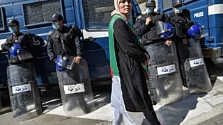 متظاهرة جزائرية تسير أمام أفراد الشرطة الذين وضعوا كمامات واقية خلال الحراك الأسبوعي بالعاصمة الجزائر. 06/03/2020