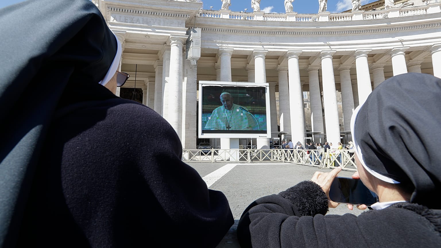 Nuns watch Pope Francis on a giant screen as he delivers the Angelus, in St. Peter's Square, at the Vatican, Sunday, March 8, 2020.