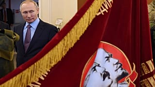 Russian President Vladimir Putin looks at a Soviet era banner depicting Soviet Union founder Vladimir Lenin and Soviet dictator Joseph Stalin 