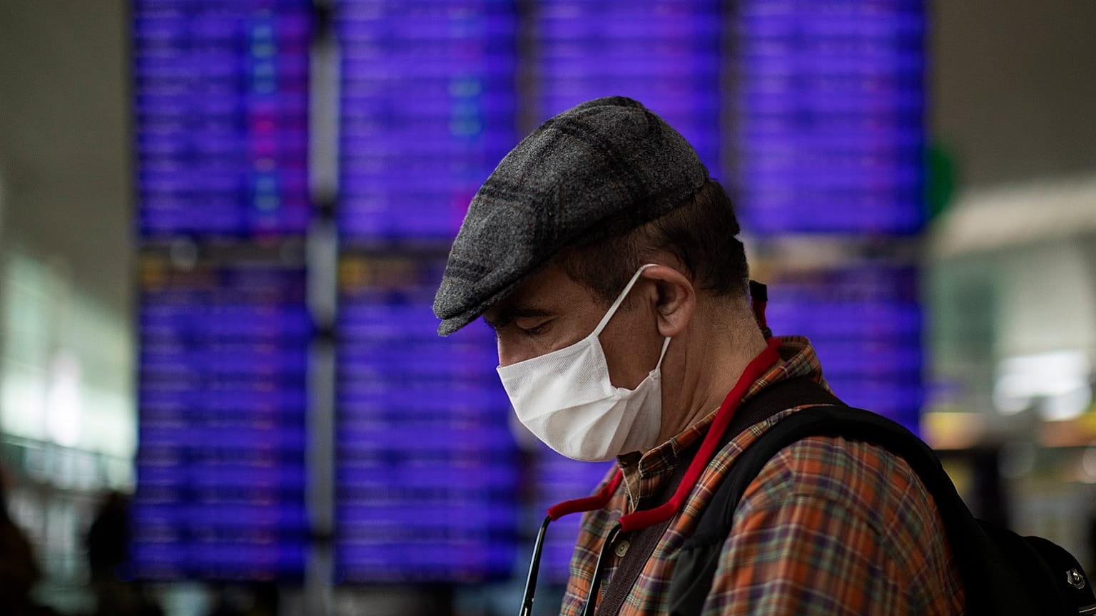 A man looks at his phone in front of the information screen at Barcelona airport, Spain, Thursday, March 12, 2020