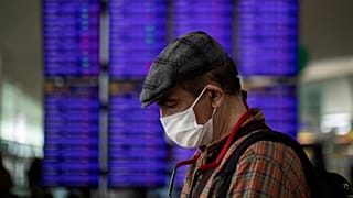 A man looks at his phone in front of the information screen at Barcelona airport, Spain, Thursday, March 12, 2020