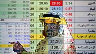 رجل أعمال سعودي يتحدث مع أخرين وخلفه شاشة كبيرة للسوق المالي في المصرف الوطني العربي بالعاصمة الرياض. 12/12/2019