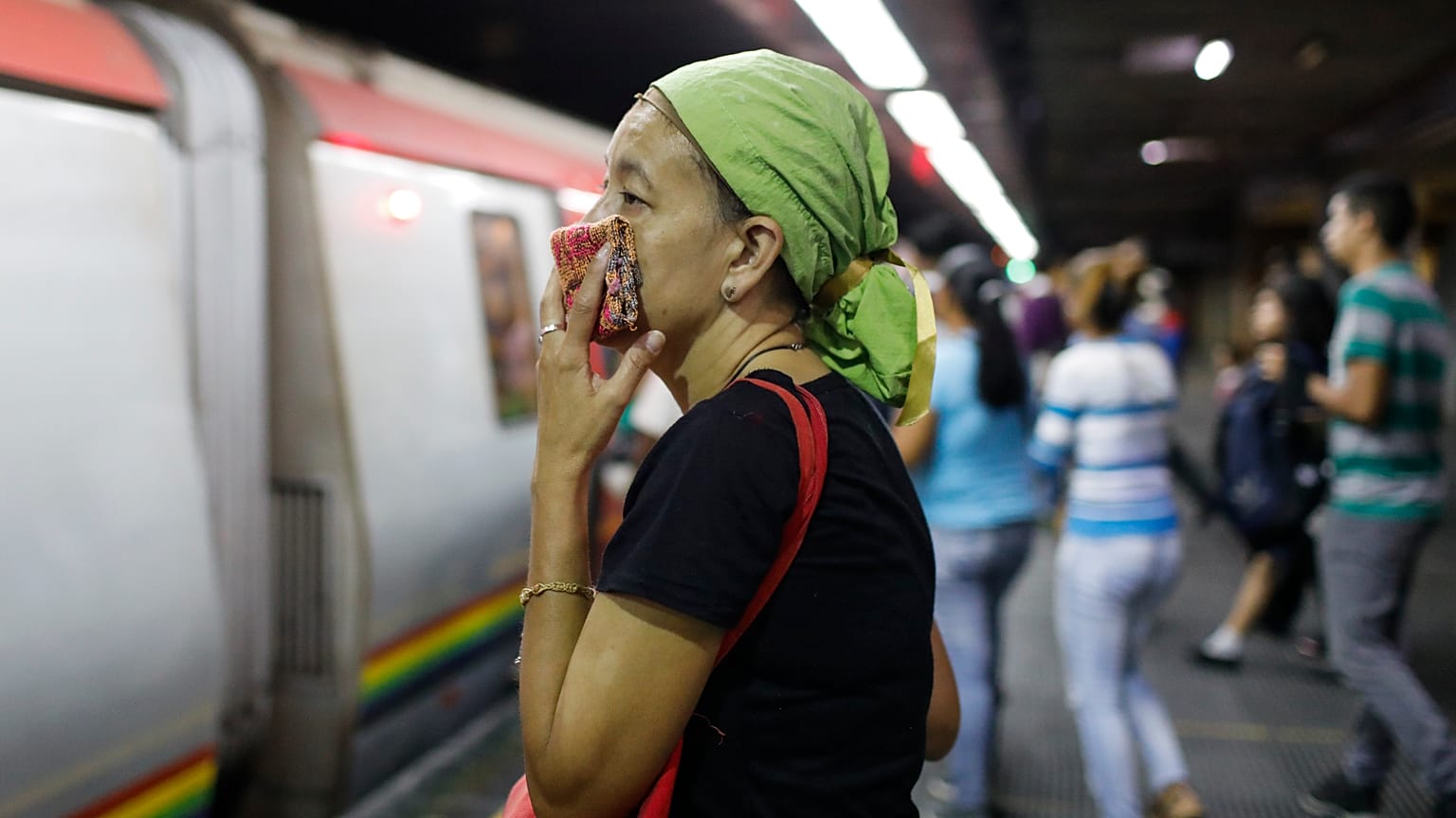A woman covers her mouth and nose with a wash cloth on a subway platform in Caracas, Venezuela, Friday, March 13, 2020. 