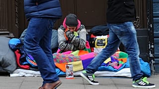 Pedestrians walk past a homeless man in the UK.