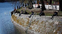 People sit in the sun on the banks of the Landwehr Canal in Berlin's Kreuzberg district on March 22, 2020,