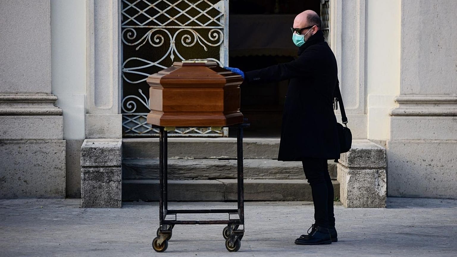 Un homme posant une main sur le cerceuil de sa mère à Bergame, le 20 mars 2020