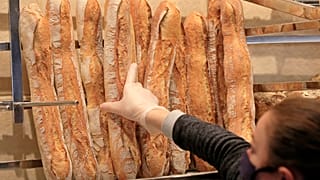 A vendor wearing a protective mask takes a baguette at a bakery in Paris, Monday, March 23, 2020.