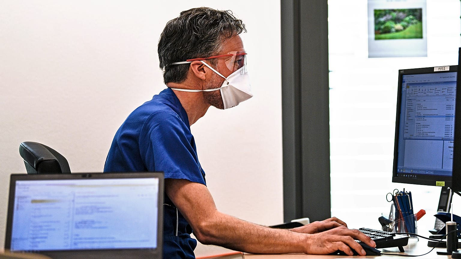 COVID-19'dan korunmak için yüz maskesi takan bir doktor, 2020 yılında Almanya'nın Essen kentindeki ofisinde bilgisayar başında çalışıyor.