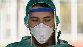 A healthcare worker dressed in protective gear waits for drivers at a drive-through testing. (Photo by CESAR MANSO / AFP)