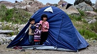 Children stand outside a tent in the village of Petra on the northeastern Aegean island of Lesbos, Greece, Friday, March 27, 2020