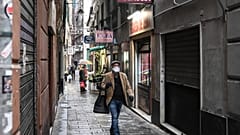A resident wearing a protection mask carrying a shopping bag walks past shops as they close up under the lockdown in Genoa, Italy, March 13, 2020.