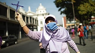 A woman holds up a cross as she tries to follow a statue of Jesus passing by during Holy Week in Caracas, Venezuela, April 8, 2020