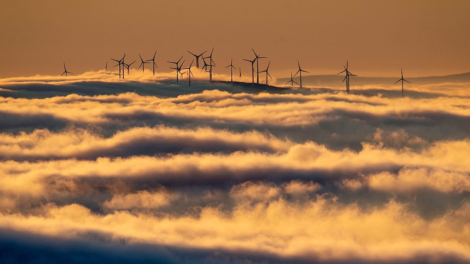 Wind turbines stand on a hill and are surrounded by fog and clouds in the Taunus region near Frankfurt, Germany