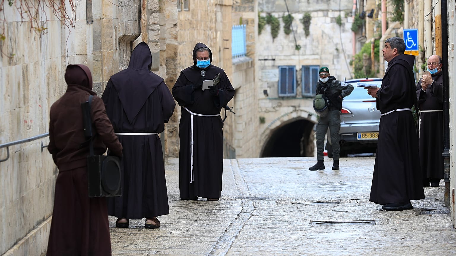 عدد من رجال الدين الفرنسيسكان بالقدس القديمة يصلون وهم يضعون أقنعة واقية من فيروس كورونا ويظهر في أقصى الصورة أفراد من الشرطة الإسرائيلية في الجمعة العظيمة.10/04/2020