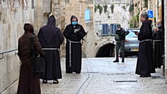 عدد من رجال الدين الفرنسيسكان بالقدس القديمة يصلون وهم يضعون أقنعة واقية من فيروس كورونا ويظهر في أقصى الصورة أفراد من الشرطة الإسرائيلية في الجمعة العظيمة.10/04/2020