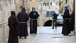 عدد من رجال الدين الفرنسيسكان بالقدس القديمة يصلون وهم يضعون أقنعة واقية من فيروس كورونا ويظهر في أقصى الصورة أفراد من الشرطة الإسرائيلية في الجمعة العظيمة.10/04/2020