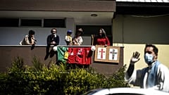 People stand on their balcony as Father Nuno Westood travels aboard a convertible Smart