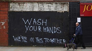 A man walks his dog past graffiti calling for people to wash their hands to combat the spread of the coronavirus, in Belfast, Northern Ireland, Monday March, 30, 2020