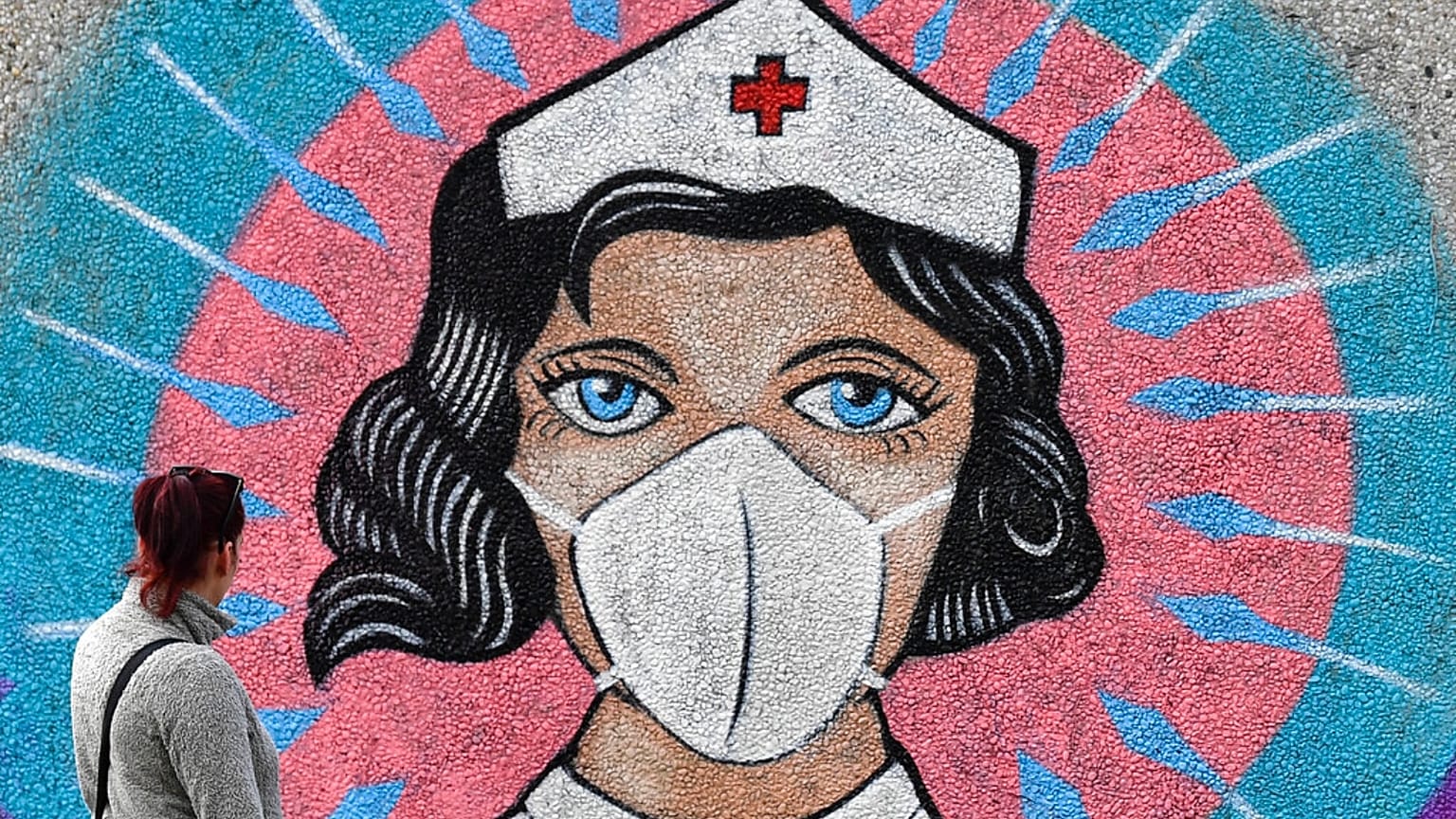 A woman looks at a coronavirus graffiti by street artist 'Uzey' showing a nurse with a face mask on a wall during a walk in Hamm, Germany, on Easter Monday, April 13, 2020.
